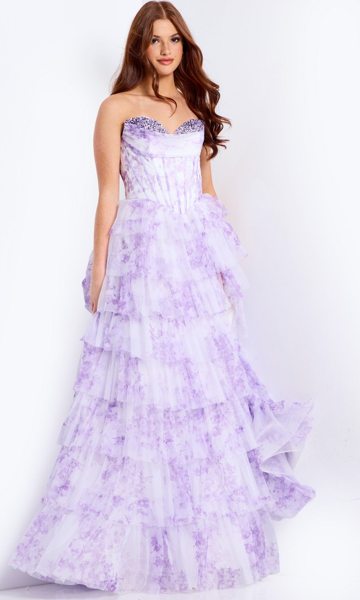 A woman models the Jovani 47440 long prom dress, featuring a strapless corset bodice and lavender tiered skirt with sparkling embellishments and floral print, standing against a plain white background.